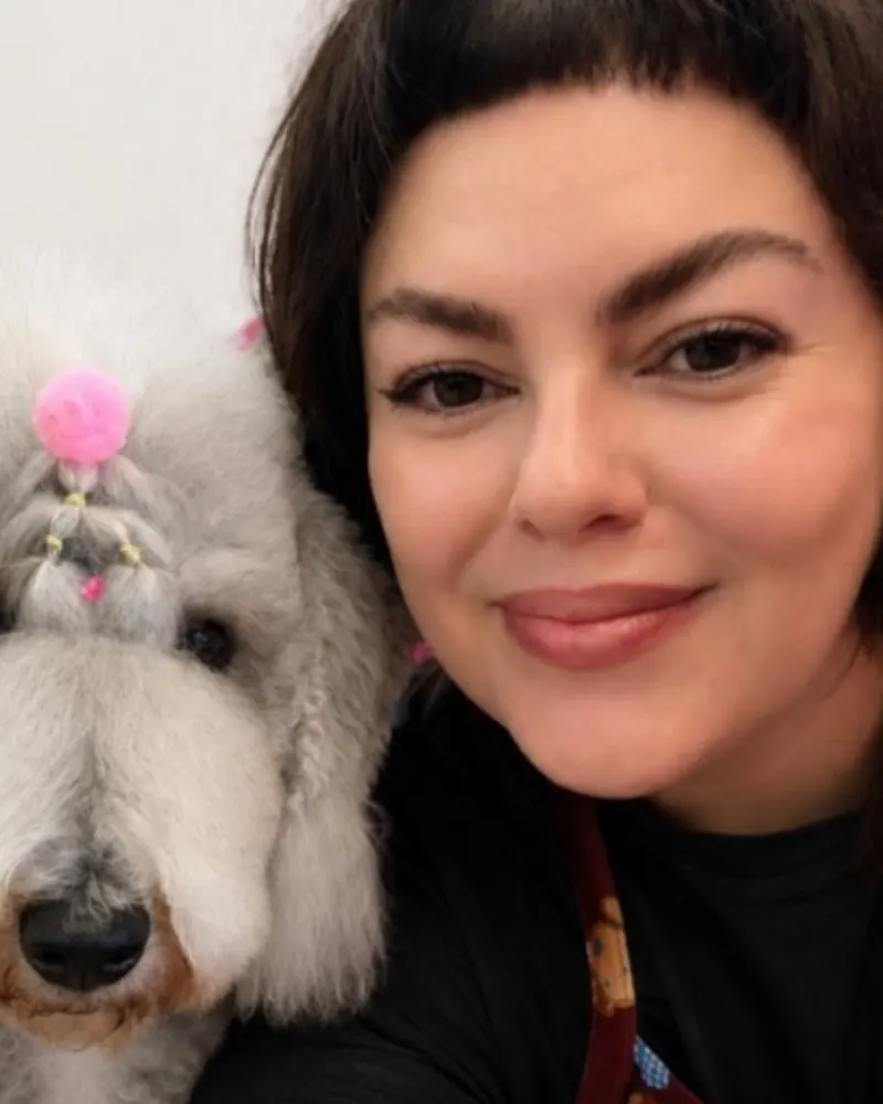Dey smiling next to a white dog with a pink topknot bow.